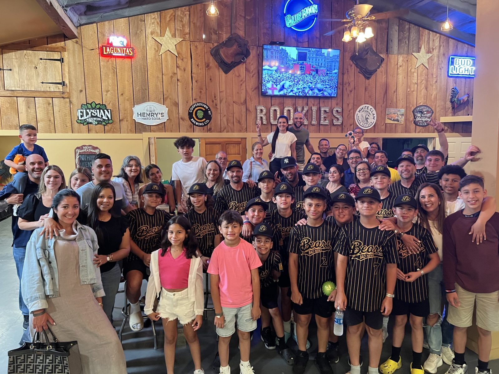 A youth baseball team in pinstripe jerseys with their parents and siblings at a team party in the Clubhouse